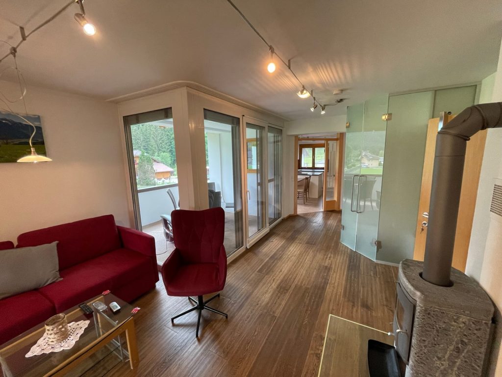 Wohnzimmer des Appartements mit Kaminofen, Sofa und Zugang zum Balkon